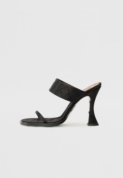 Black high-heeled sandals with a quilted upper strap and a thin ankle strap. Features a unique sculpted heel shape. Smooth texture.