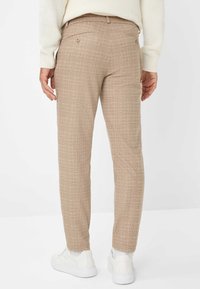 Beige geruite broek met slim fit, voorzien van een achterzak en subtiele textuur. Gecombineerd met witte sneakers.