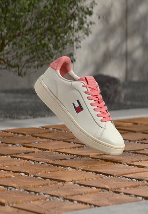 Bijela tenisica s ružičastim detaljima, ima gornji dio od glatke kože, ružičaste vezice i mali logotip na bočnoj strani.