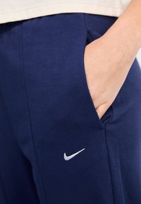 Tumesinine sportlikud püksid pehme tekstuuriga, küljetasku ja ees väike valge Nike logo.