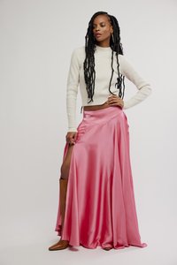 Falda larga de satén rosa con una abertura alta y una cintura ceñida, combinada con un suéter de canalé beige claro y botas marrones hasta la rodilla.