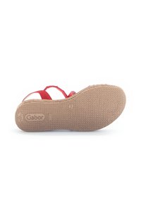 Red sandal with a textured rubber sole featuring straps. Bottom view shows brand logo and a durable, non-slip surface design.