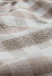 Austs aužamais audums ar gaiši bēša un baltu rūtainu rakstu, ar mīkstu tekstūru un smalku spīdumu, relaksētā izskatā.