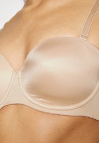 Beige polstret bh med glatt satengfinish, underwire støtte, justerbare stropper og en sømløs design for en slank silhuett.