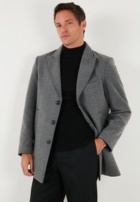 Sivi plašč iz mešanice volne, enorazni kroj, ovratnik z zarezami, trije sprednji gumbi, dva stranska žepa in prsni žep.