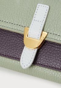 Borsa in pelle verde e viola con una tracolla azzurro chiaro e hardware dorato. Presenta un dettaglio decorativo di chiusura.