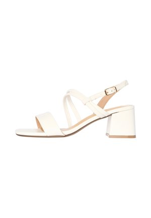 Sandale blanche à bout ouvert avec talon bloc, bride de cheville ajustable avec boucle dorée et brides croisées sur le dessus du pied.