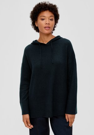 Dunkelgrüner, übergroßer Hoodie aus weichem Stoff, mit einer Kapuze mit Kordelzug, gerippten Bündchen und Saum. Das Model trägt dunkelblaue Hosen.