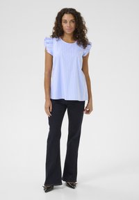Blusa a righe blu e bianche con maniche svasate, abbinata a jeans a zampa d'elefante scuri e scarpe nere con punta appuntita. Tessuto morbido.