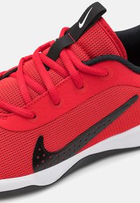 Roter Sportschuh mit einem Mesh-Obermaterial, schwarzen Akzenten, prominenten Nike-Swoosh, strukturierten Oberflächen und einer weißen Zwischensohle mit einer schwarzen Außensohle.