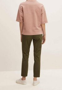 Rosafärgad bomullstopp med kort ärm, kombinerad med olivgröna avsmalnande byxor, som har en avslappnad passform, samt vita sneakers.