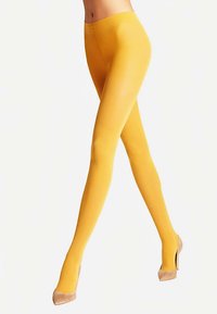 Collant gialli opachi con una texture liscia e lucida, abbinati a décolleté beige. Il design è aderente e senza cuciture in vita.