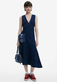 Jeansklänning med djup V-ringning, omslagsdesign och utsvängd nederkant. Matchad med en liten jeans crossbody-väska och röda sneakers.