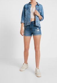 Denim jacket with a relaxed fit, light blue color, paired with light blue distressed shorts. White sneakers with a textured sole complete the outfit.