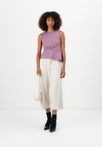 Lilac fitted tank top with a peplum design, paired with cream wide-leg trousers, black high heels, and a white handbag. Plain background.