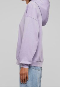 Sudadera de color púrpura claro con un bolsillo tipo canguro, puños y bajo acanalados. Presenta una capucha con cordón y un corte relajado. Fabricada en una suave mezcla de algodón.