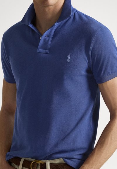 Blue cotton polo shirt with a collared neck and a small embroidered logo on the left chest. Textured fabric with short sleeves and a straight fit.