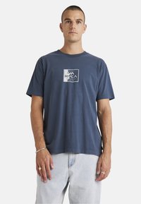 Navy blue cotton T-shirt with short sleeves, crew neck, and a front logo detail in white. Relaxed fit with a hemline that sits at the waist.