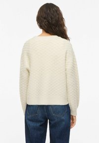 Pull de couleur crème avec un motif nid d'abeille texturé, ourlet et poignets côtelés, assorti à un jean bleu foncé. Design décontracté, tissu doux.