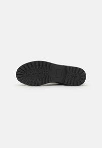 Suela de zapato de goma negra con un patrón profundo y estriado que presenta diseños florales en relieve y una sección rectangular plana. Superficie texturizada para agarre.