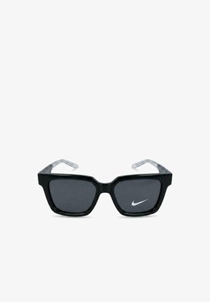 Occhiali da sole neri con montatura quadrata, lenti scure e aste trasparenti, con un piccolo logo bianco Nike Swoosh sulla lente destra.
