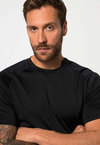 Černé sportovní tričko s kulatým výstřihem, krátkými rukávy a hladkou texturou. Obsahuje nenápadné logo na hrudi a kontrastní švy.