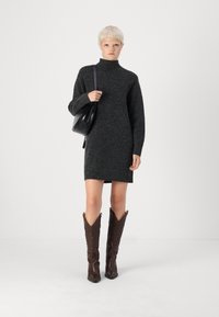 Vestido de malha cinza escuro com gola alta e mangas longas, combinado com uma mala preta brilhante e botas de cowboy em couro castanho.