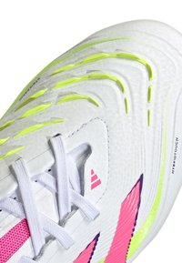 Witte sportieve sneaker met textuurmaterialen, neongele accenten, roze strepen en witte veters; beschikt over een hybride ontwerp met duidelijke patronen.