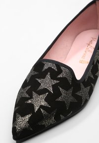 Primer plano de un zapato plano negro puntiagudo con patrones de estrellas de glitter plateado y una plantilla rosa.