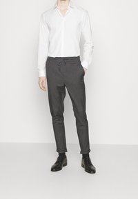 Pantaloni jogger affusolati grigi con vita regolabile, realizzati in tessuto morbido. Indossati con una camicia bianca button-up e scarpe nere.