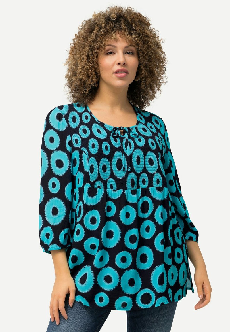 Blauw en teal gestippeld blouse met een ronde halslijn, strikdetail en driekwart mouwen, gemaakt van lichtgewicht stof. Kenmerkend zijn de ronde ontwerpen.