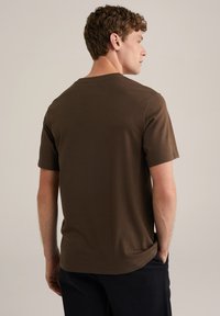 Hnědé tričko s krátkým rukávem a volným střihem, vyrobené z měkkého materiálu, s klasickým kulatým výstřihem a minimalistickým designem.