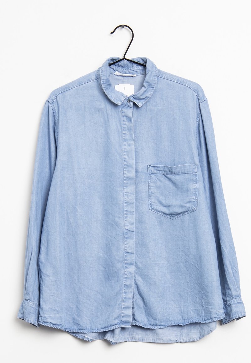 Chemise bleu clair à manches longues avec col et poche poitrine suspendue sur un cintre noir sur fond blanc.