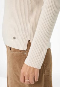 Pull côtelé beige clair à manches longues et fentes sur les côtés. Assorti à un pantalon en velours côtelé marron, avec un détail de poche subtil.
