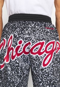 Mustat ja valkoiset pilkulliset shortsit, joissa on punainen "Chicago" -teksti edessä. Shortsien päällä oleva henkilö on pukeutunut valkoiseen paitaan, ja elastinen musta vyötärönauha on näkyvissä.