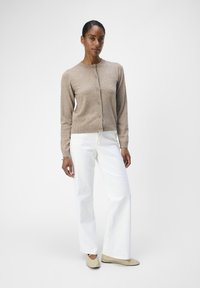 Beige strikket cardigan med rund hals og knappestolpe, kombinert med hvite vide bukser og lyse flate sko. Glatt tekstur.