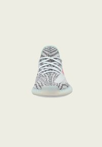 Sapatilha cinza claro com um upper em malha texturizada e padrões mais escuros, atacadores brancos e sola de borracha translúcida. Acento em vermelho.