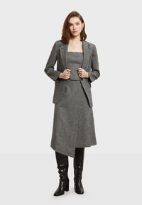 Sivý vlnený blazer s klopami, doplnený zodpovedajúcim skráteným topom a sukňou. Oblečenie má štruktúrovaný povrch a je doplnené čiernymi čižmami po kolená.