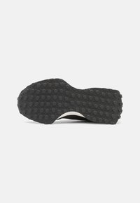 Semelle de chaussure en caoutchouc noir présentant une surface texturée avec des motifs circulaires et un bord blanc cassé. Forme arrondie avec un design antidérapant.
