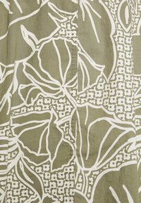 Tela verde con llamativos patrones florales blancos con contornos detallados y motivos geométricos. Textura suave con un brillo sutil.