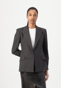 Blazer croisé en tissu gris foncé avec des rayures blanches. Présente un large col, deux poches avant et des boutons noirs.