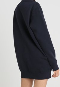 Marinblå sweatshirt gjord av mjukt, strukturerat tyg. Har långa ärmar, rundad halsringning och en avslappnad passform. Nederkanten når till mitten av låret.