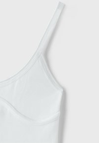 Haut caraco blanc avec fine bretelle et détail de couture incurvée sur fond en tissu doux.