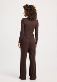 Bruine set met lange mouwen en broek, gemaakt van zachte stof. Het topje heeft een ronde halslijn en een aansluitend ontwerp; de broek heeft een ontspannen pasvorm.