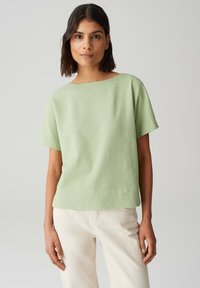 Haut court à manches courtes texturé vert clair, avec une coupe ample et un large col, associé à un jean écru. Tissu doux et design décontracté.