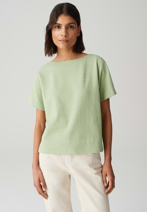 Haut court à manches courtes texturé vert clair, avec une coupe ample et un large col, associé à un jean écru. Tissu doux et design décontracté.