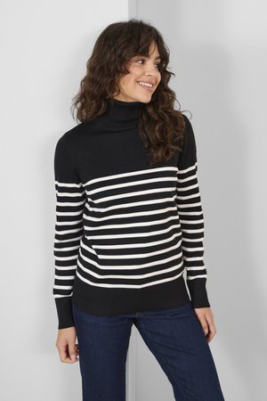 Black and white striped turtleneck sweater with ribbed cuffs and hem, featuring a fitted design and long sleeves, paired with blue jeans.