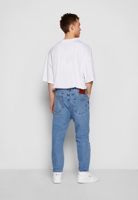 Jean en denim bleu clair avec une coupe décontractée, d�étails sur les poches arrière, associé à un t-shirt blanc ample et des baskets blanches.