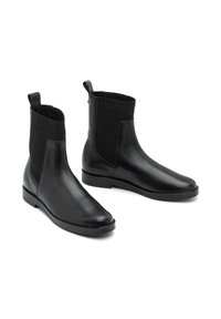 Botines de cuero negro con parte superior de tejido acanalado, punta redondeada, suela plana y una lengüeta en el talón para facilitar el calce.