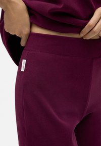 Joggers burdeos texturizados con una cinturilla ancha y una pequeña etiqueta de marca. Primer plano de la tela que resalta el diseño y los detalles.